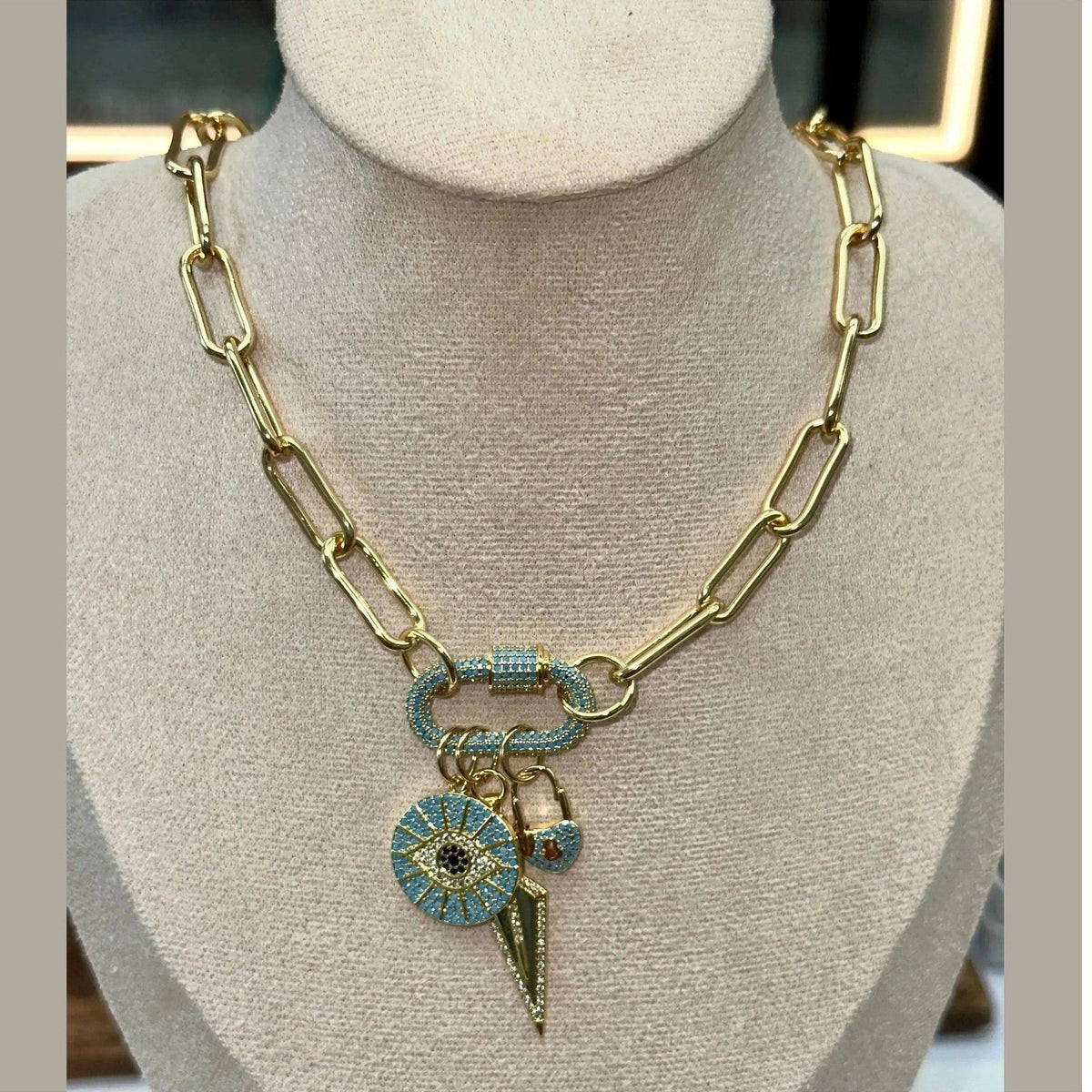 Close-up of Daphne Trio Charms Necklace showing evil eye, padlock, and spike details on gold chain