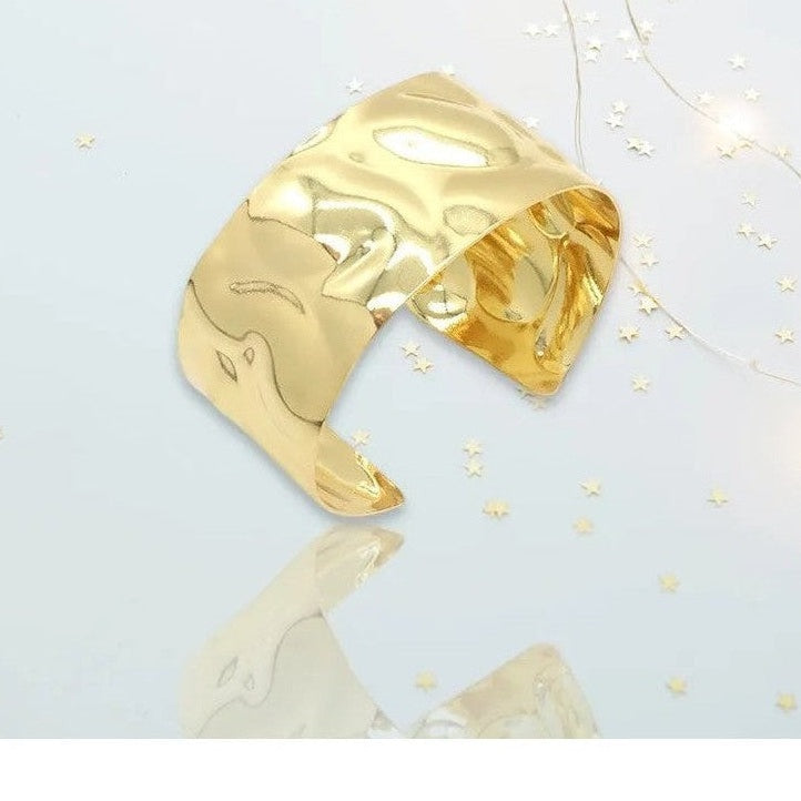 Polished fluid undulating gold cuff bracelet on reflective background
